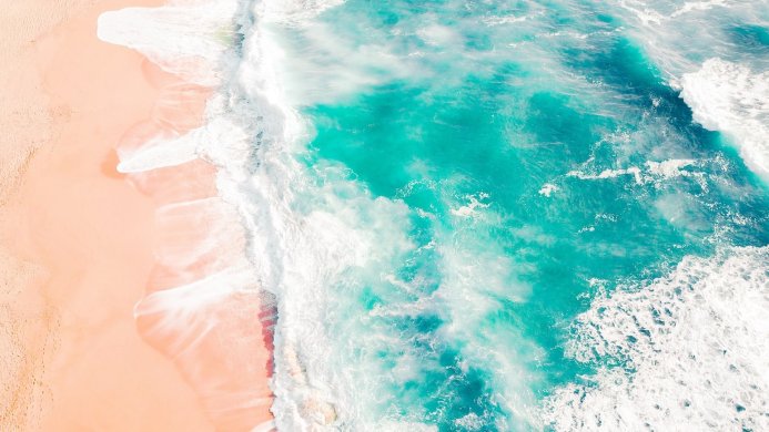 Aerial view of waves crashing on a sandy beach, turquoise water and white foam