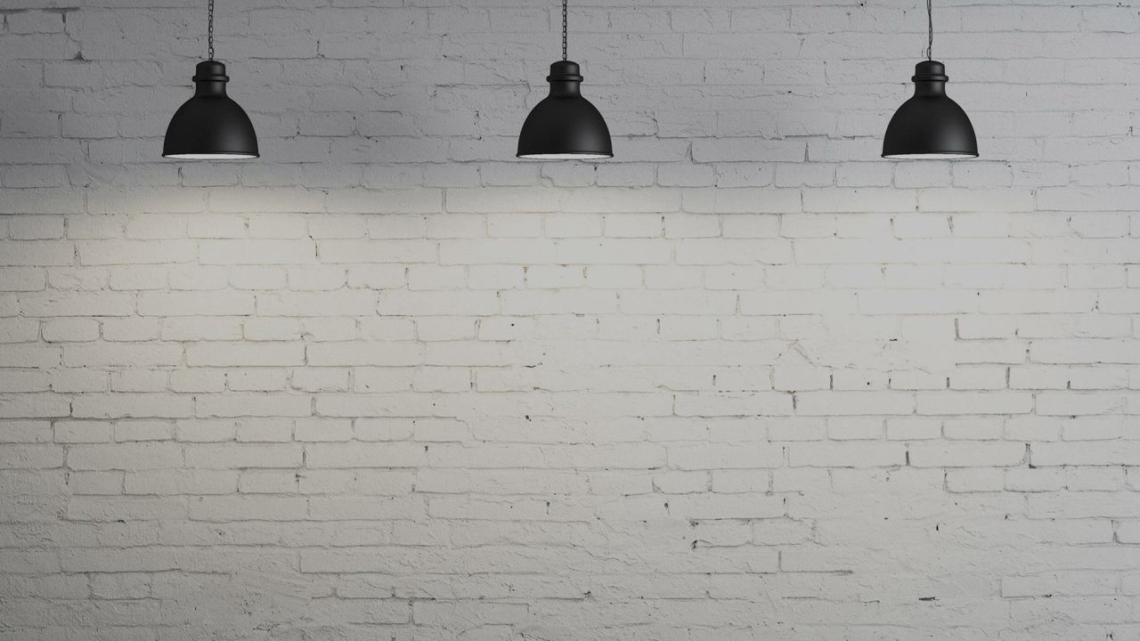 Three black lamps hanging above white brick wall