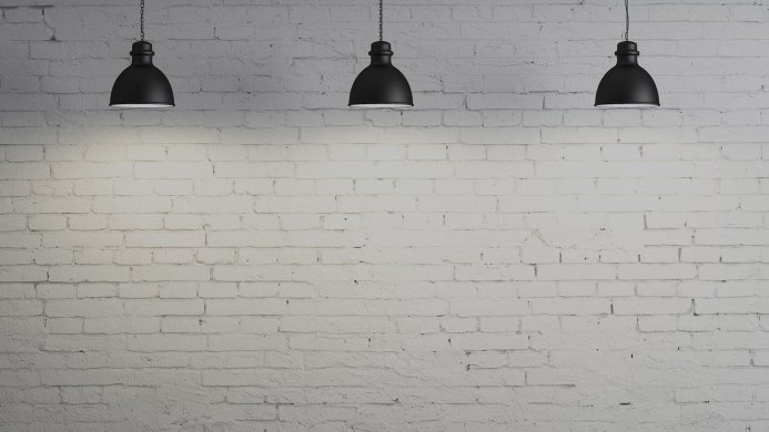 Three black lamps hanging against a white brick wall
