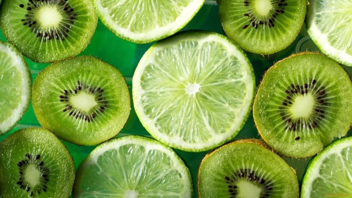 Slices of kiwi and lime on a green surface, showing their textures and vibrant colors