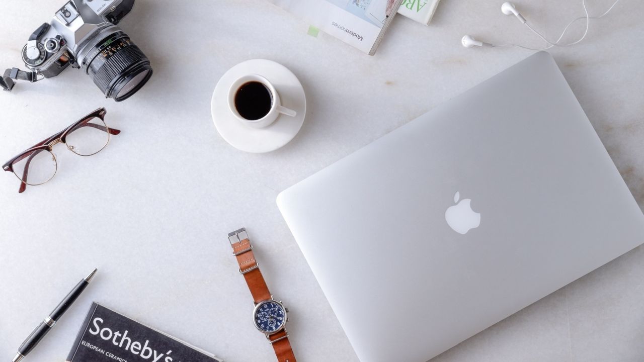 Flat lay of laptop camera coffee glasses watch on white desk