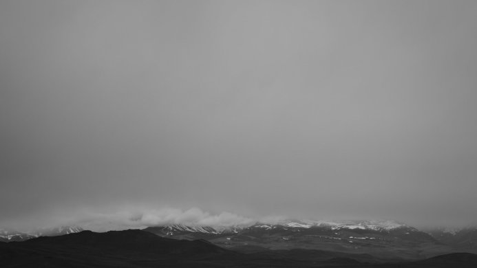 A monochrome image of mountains partially obscured by low-hanging clouds