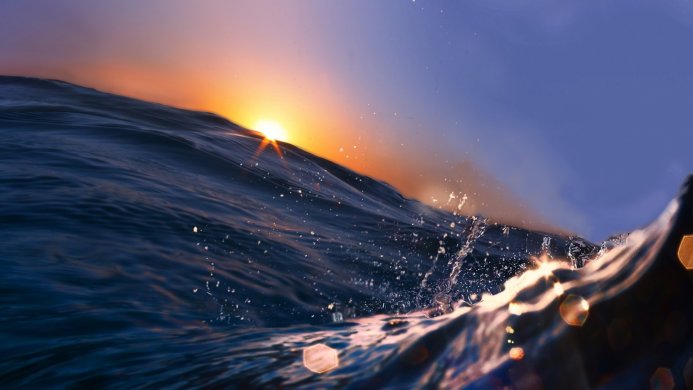Ocean wave at sunrise with blue and orange hues