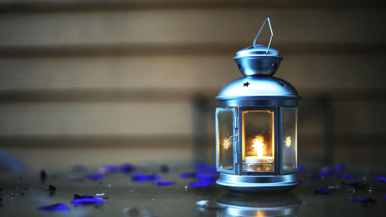 Lantern with candle and blue petals on surface