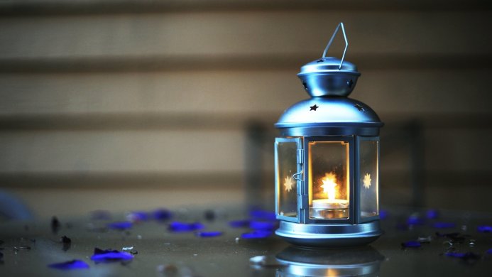A silver lantern with a burning candle and blue flower petals around it