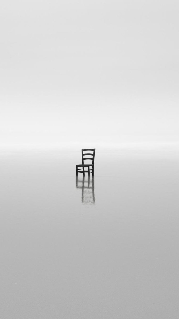 A single chair sits on a reflective surface in a minimalist landscape