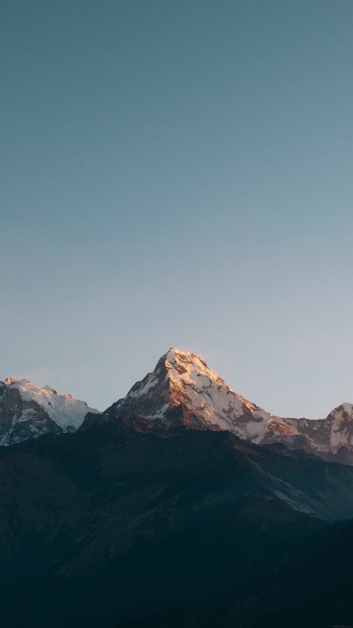 A majestic mountain peak, partially covered in snow, illuminated by the sunrise against a blue sky