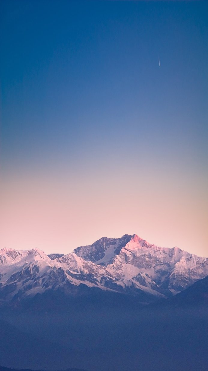 Snowy mountain range with a blue sky gradient and pink sunrise