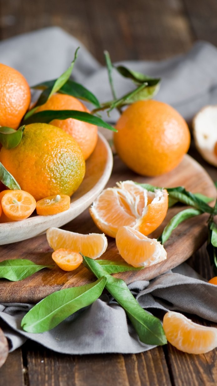 Close-up of tangerines and kumquats with green leaves on a wooden surface