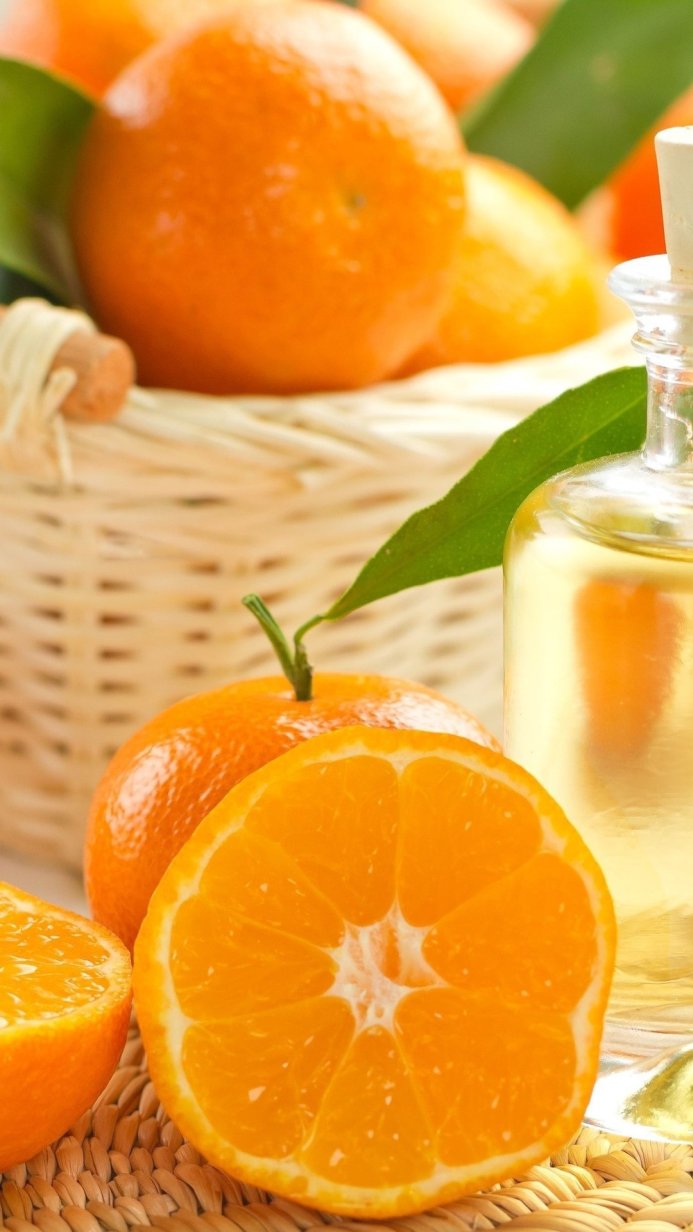 Close up of tangerines, sliced tangerine, and tangerine oil in a glass bottle