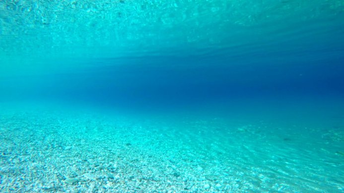 Underwater view of a seabed with clear turquoise water and white pebbles