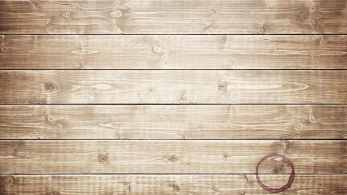 A close-up of weathered wooden planks with a dark ring stain in the lower right corner