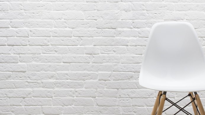 A white modern chair stands against a white brick wall