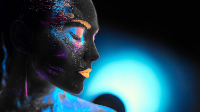 Profile of a woman with ultraviolet makeup on her face and body, glowing in blue and pink
