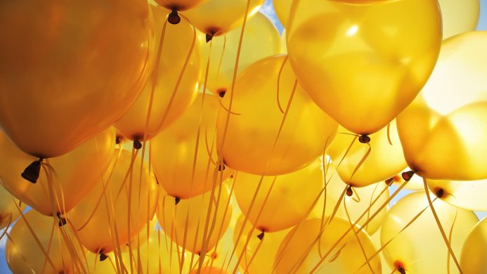 A cluster of yellow balloons against a light blue sky