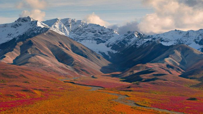 A landscape view of mountains with snow-capped peaks and autumn foliage in orange and red hues