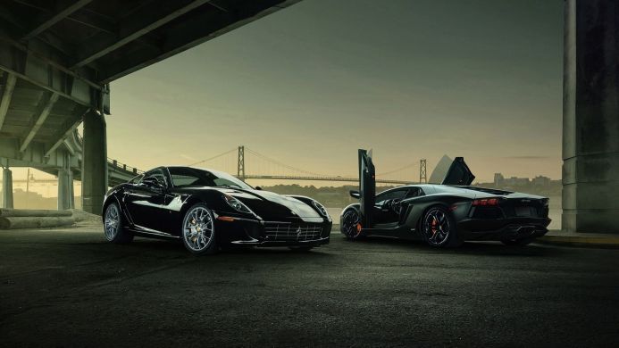 A black Ferrari and Lamborghini parked under a bridge with the city and bridge in the background