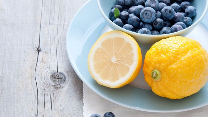 Close-up of blueberries in a bowl and lemons on a plate, wooden background