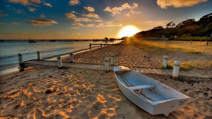 A small boat on a sandy beach at sunset, with a pier extending into the sea