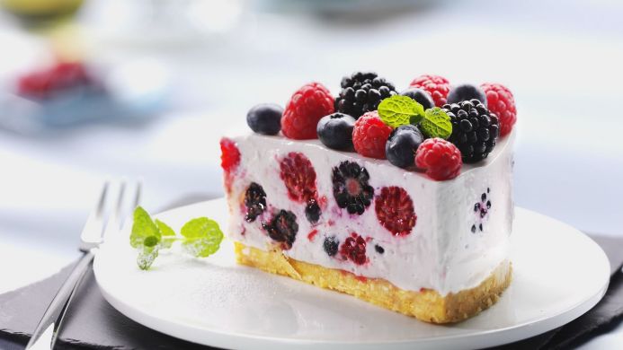 Slice of cheesecake topped with fresh raspberries, blackberries, and blueberries, garnished with mint