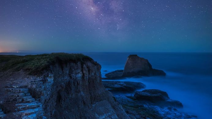 Cliffs and rock formations on the coast under a night sky full of stars
