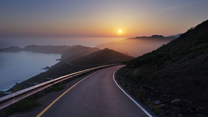 Coastal road winding through hills at sunset