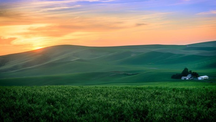 Rolling green hills under a colorful sunrise sky with a small farm
