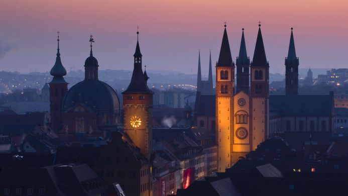 Illuminated cathedral towers at night with a cityscape backdrop under a purple sky