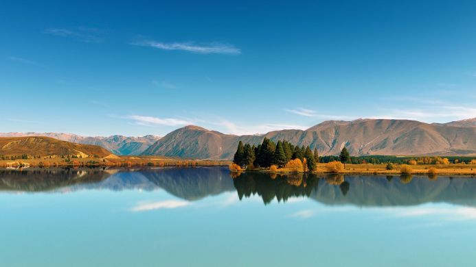 Lake with mountains and trees reflected in the water under a blue sky