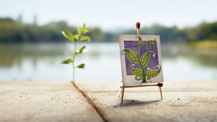 Miniature drawing on an easel with a plant in the background against a blurry lake landscape