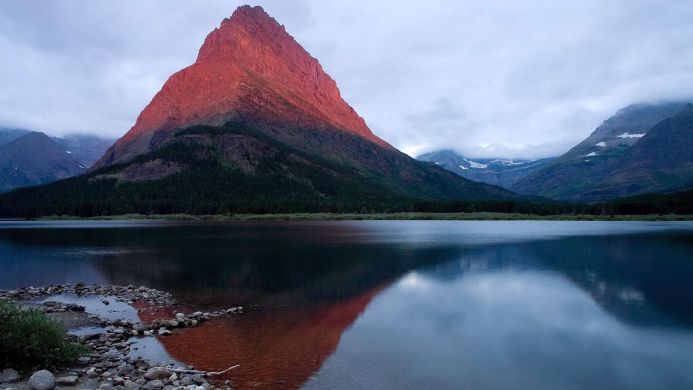 Red mountain reflecting in a lake under a cloudy sky