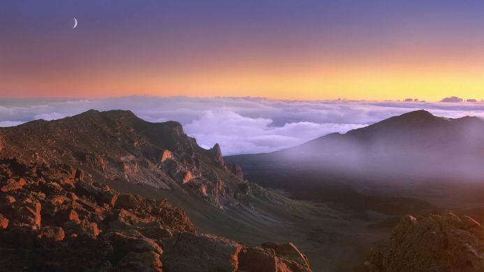 Mountain range with clouds and a crescent moon at dawn