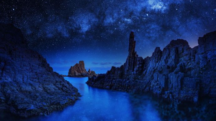 Night scene of rocky coast with starry sky and milky way reflected in the water