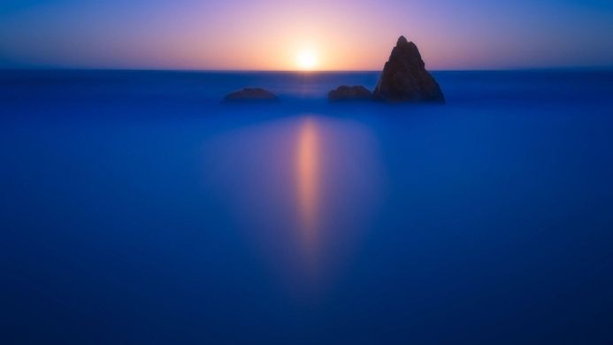 Rocks in the ocean at sunrise with a long exposure, creating a smooth, blue water surface