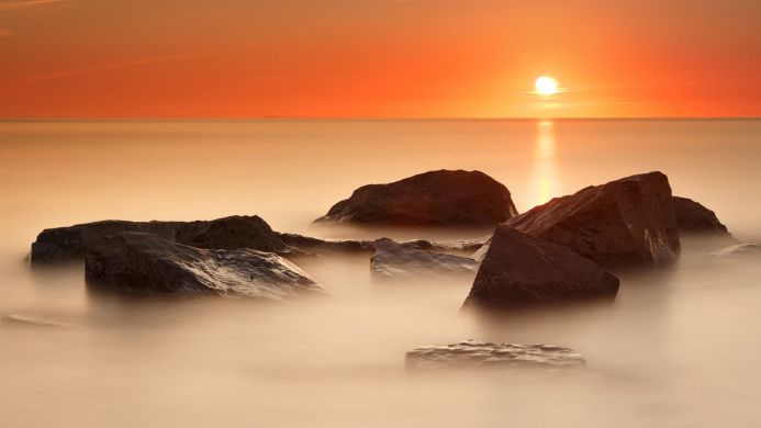 Rocks in the ocean at sunset with orange sky and smooth water
