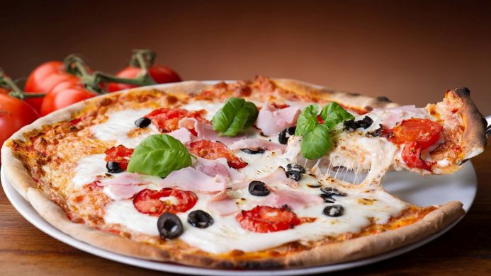 A delicious looking pizza with ham, tomatoes, basil and olives