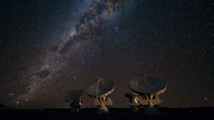 Radio telescopes under a starry night sky with the Milky Way visible