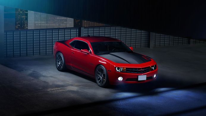 A red Chevrolet Camaro with a black hood is parked in a garage