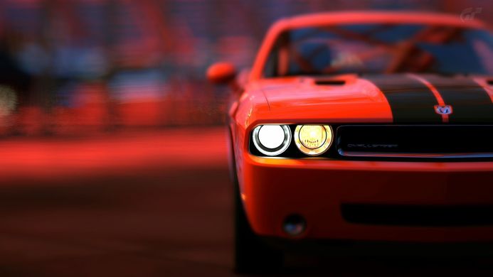 Front view of a red Dodge Challenger with black stripes, focus on the headlights
