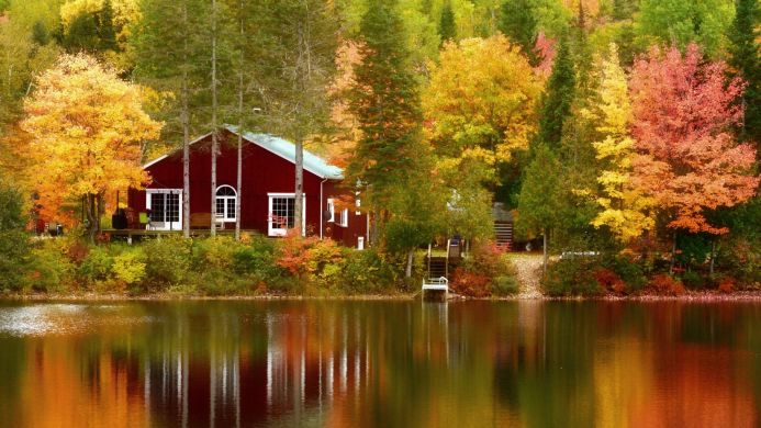 Red house near a lake surrounded by colorful autumn trees