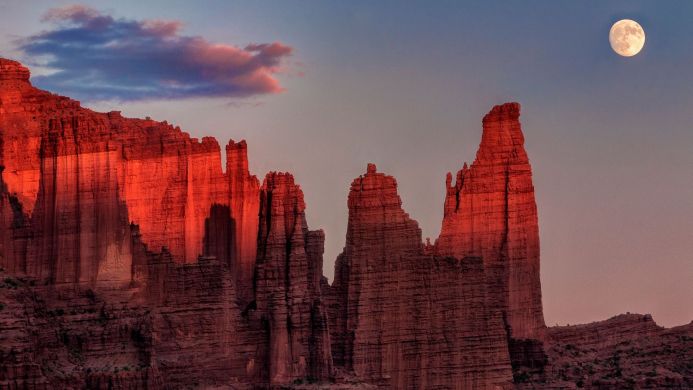 Red rock formations under a full moon at dusk