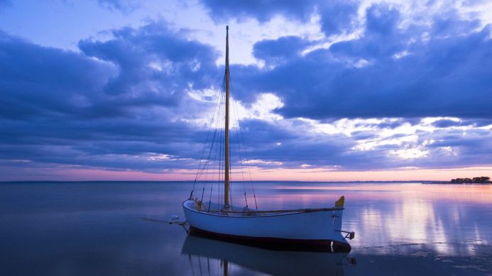 Sailboat on calm water with a dramatic blue and purple sky at sunset