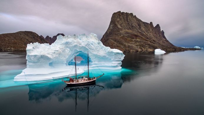 Sailboat navigating through an iceberg arch in a remote Arctic landscape