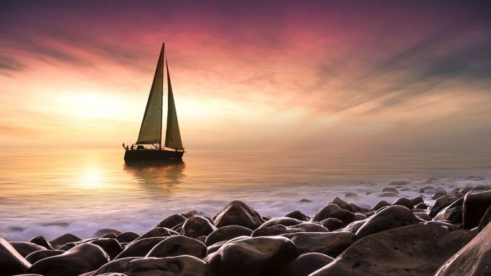 Sailboat on the sea at sunset, rocks on the shore