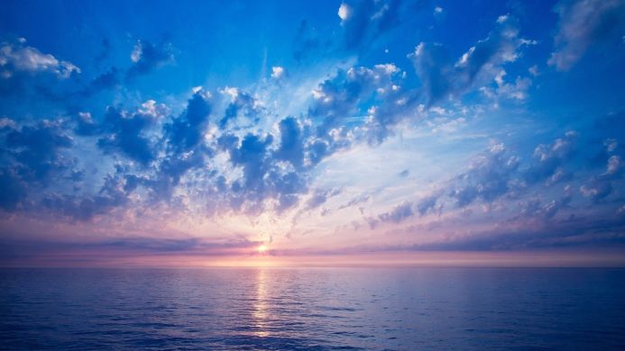 Calm sea under a cloudy sky at sunrise, with shades of blue, pink and purple