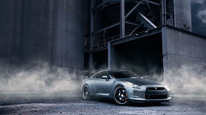 Silver Nissan GT-R in front of an industrial building with smoke