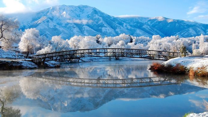 Snowy mountain landscape with a bridge over a river reflecting the mountains and sky