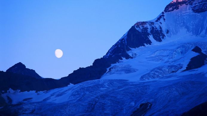 Snowy mountain with moon in the sky, captured in blue tones