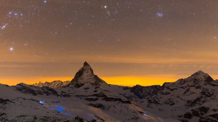Snowy mountain range under a starry night sky with orange glow