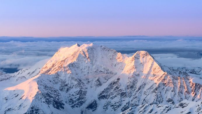 Snow-covered mountain peak with a pink sunrise and a sea of clouds in the background